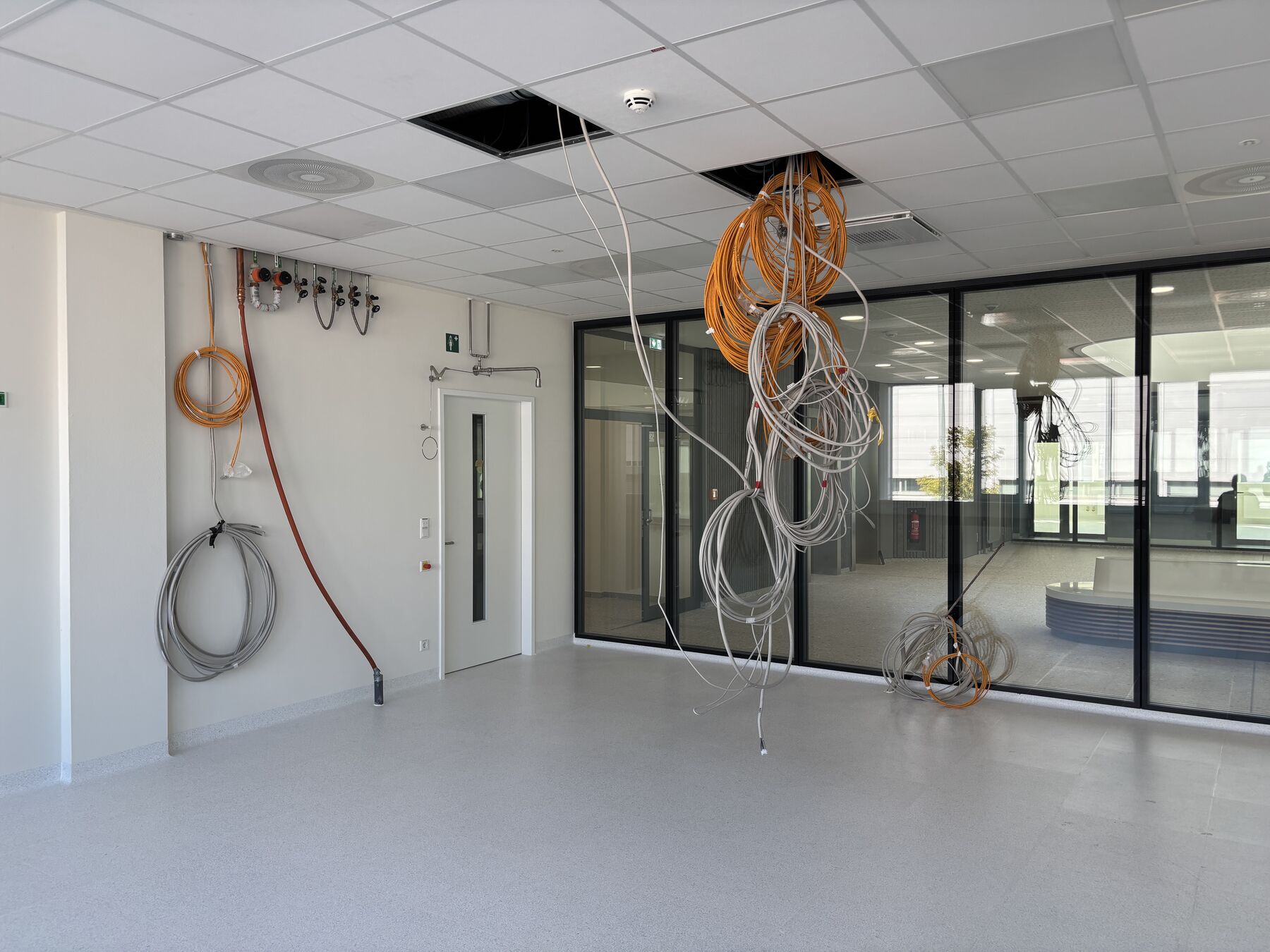 Laborraum mit aufgerollten Anschlussleitungen an der Decke, Medienanschlüssen an der Wand und Verglasung zum Atrium